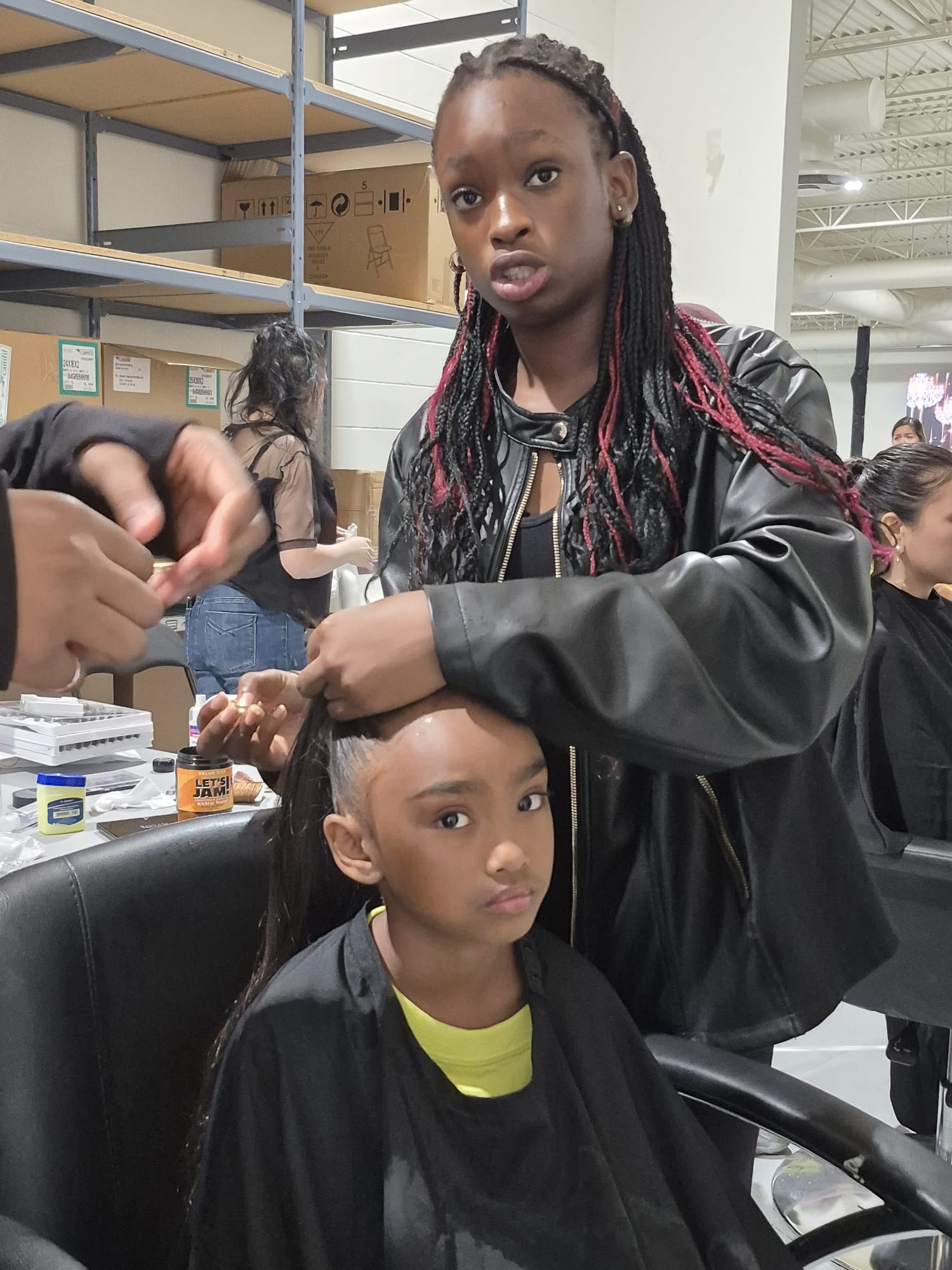A camper braids a young client's hair backstage between entrances