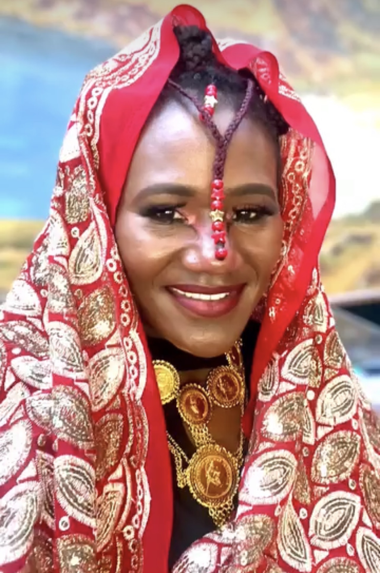 A woman in traditional red and gold Kushite dress with gold jewellery