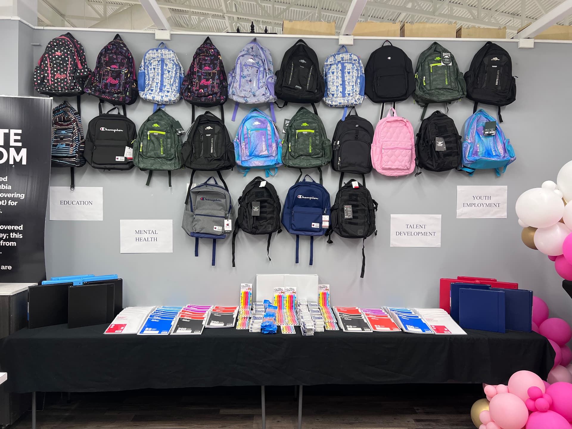 Backpacks hung on a wall beneath signs for Education, Mental Health, Talent Development and Youth Employment