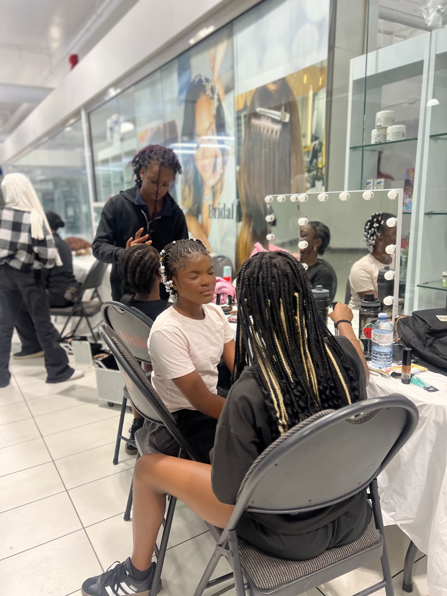 A participant braids another camper's hair beside a lit styling mirror