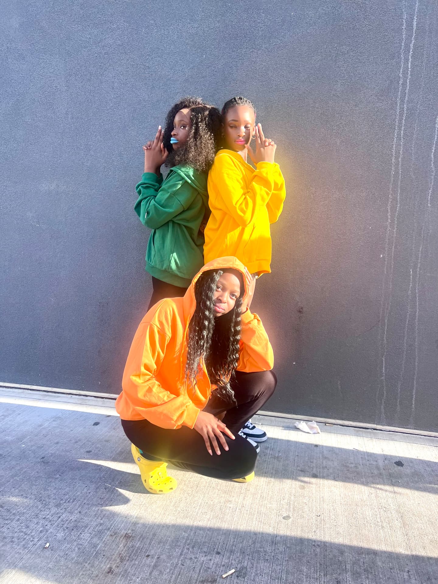 Three students in green, yellow and orange posing against a wall