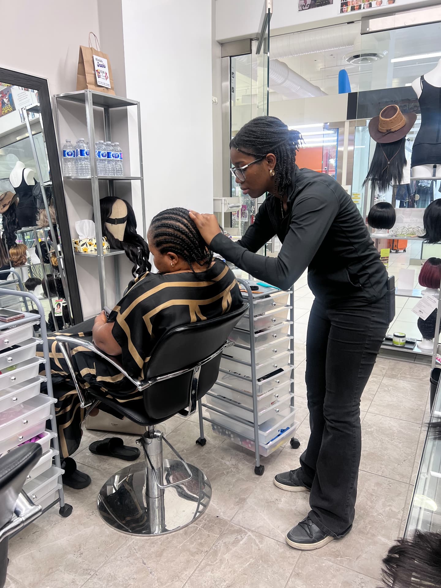 A participant practises cornrow braiding on a client in a salon chair
