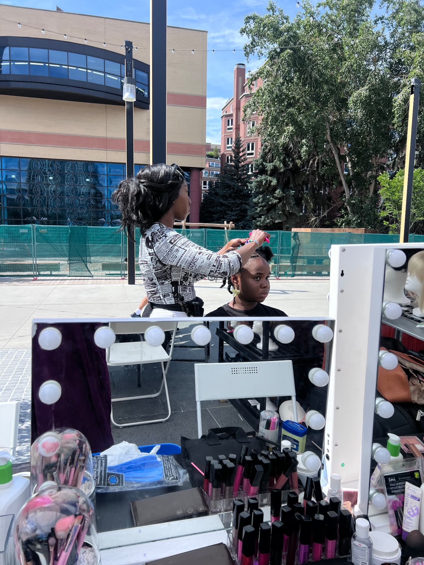 A student styles a young girl's hair at an outdoor beauty station