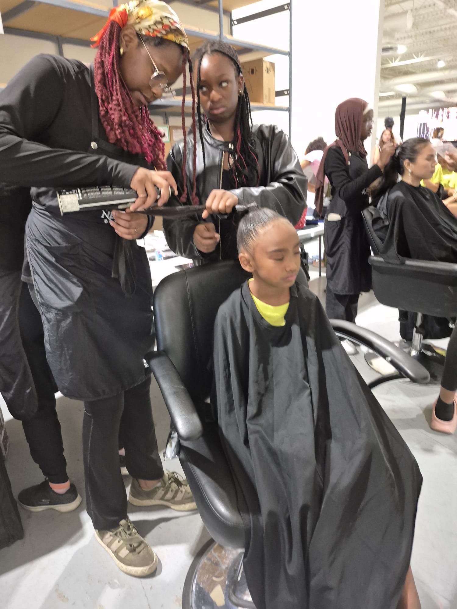 A camper sets a young client's finished hairstyle backstage
