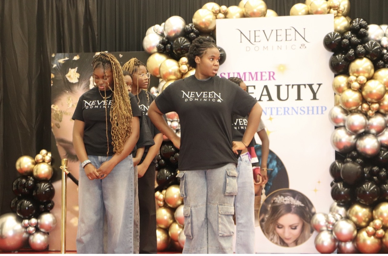 Camp participants on stage in NEVEEN DOMINIC t-shirts beneath the Summer Beauty Internship banner at the graduation celebration