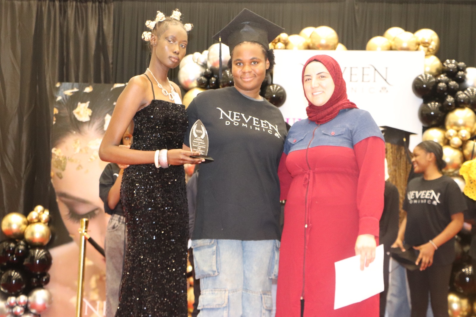 An award winner stands on stage with her trophy, flanked by her mentors