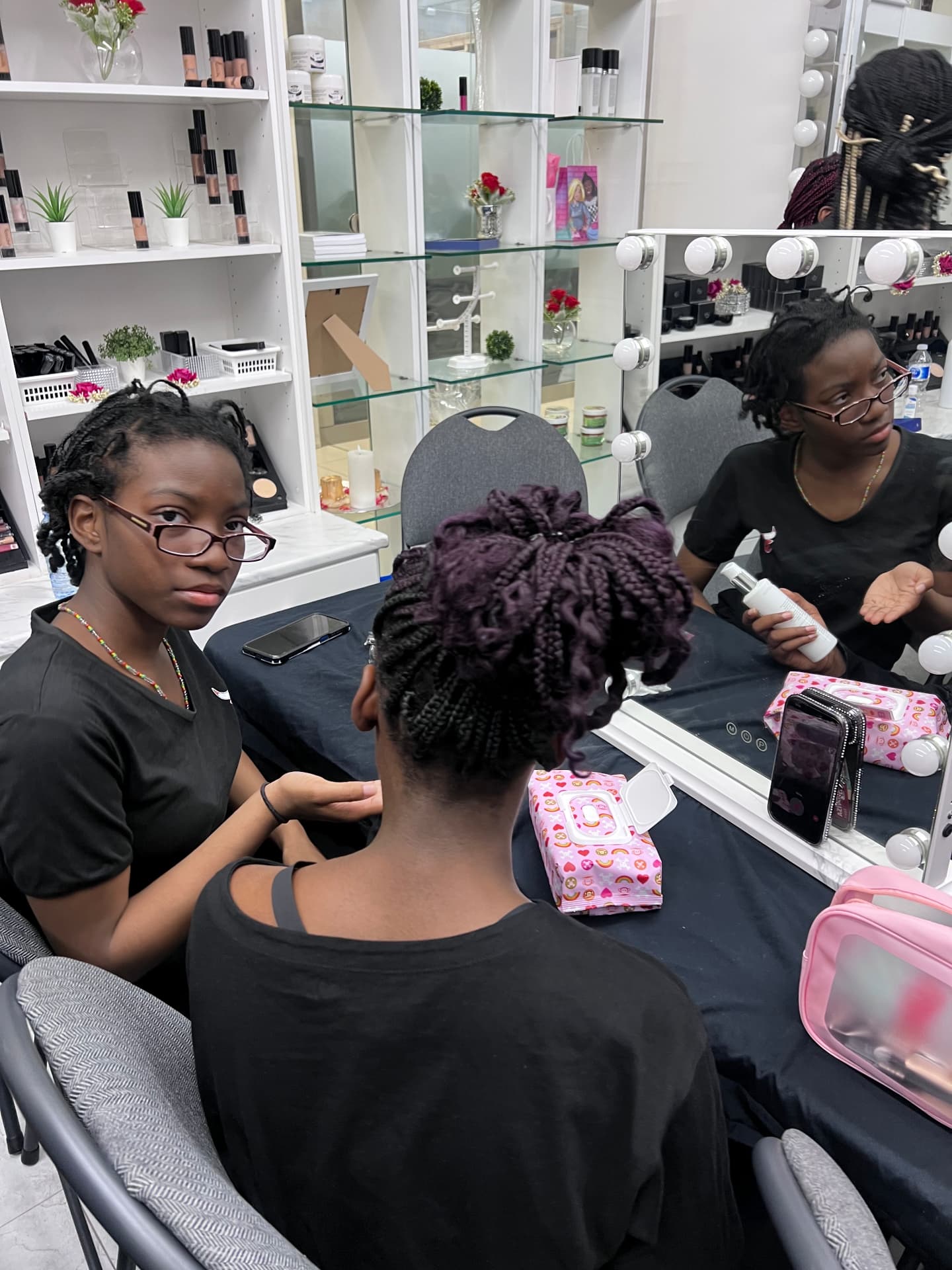 A participant has her braided updo styled at a makeup studio mirror